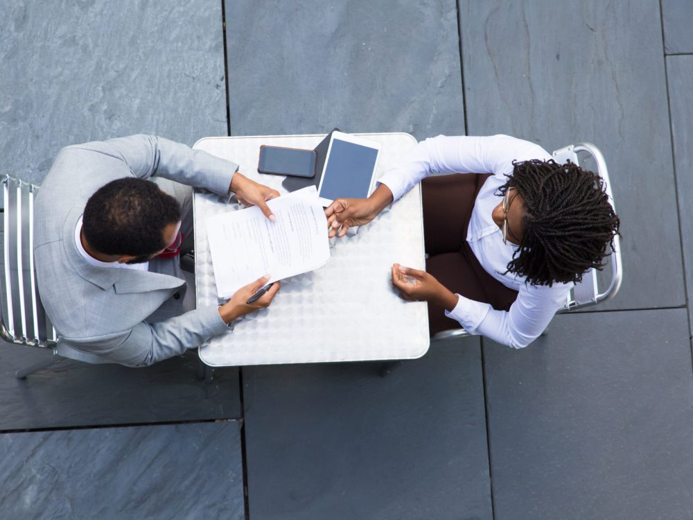 African American businesswoman passing documents to colleague African American businesswoman passing documents to colleague. Two workers reading papers while sitting at table. Business meeting concept