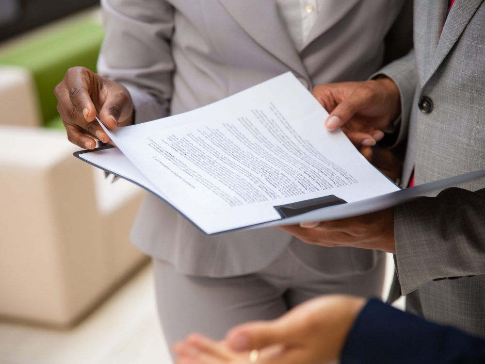 Diverse business partners reading contract together Diverse business partners reading contract together. Business man and woman wearing formal suits, standing and holding open folder with document. Agreement concept